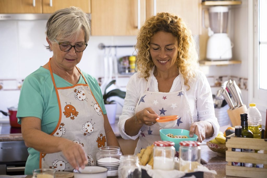 grandma-and-daughter-at-home-cooking-and-smiling-enjoying-and-have-fun-indoor-together-daughter-drinking-the-and-grandma-is-showing-how-to-cook-fish