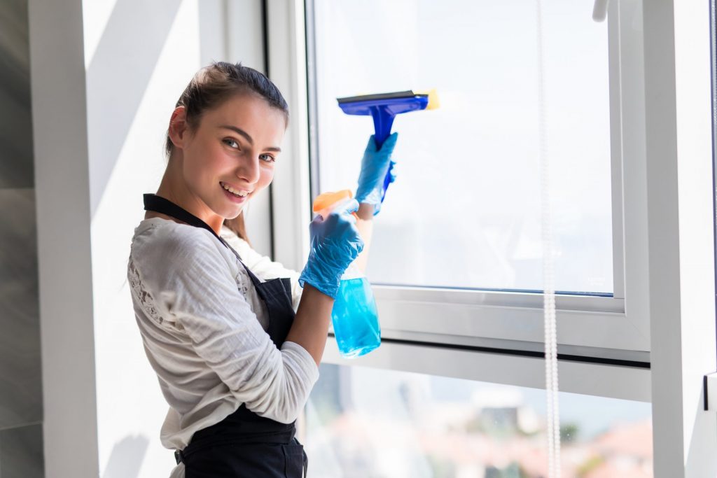 people-housework-and-housekeeping-concept-happy-woman-in-gloves-cleaning-window-with-rag-and-cleanser-spray-at-home